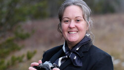 Photographer holding a vintage film camera and smiling at the camera outdoors.