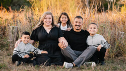 Family of five sitting together in a field of dried grass and golden light.