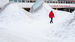 Person in bright red jacket walking across snowy landscape with geometric white structures.