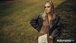 Woman in black leather jacket and neutral tones standing in overgrown field during golden hour.