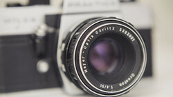 Vintage rangefinder camera with fast prime lens in sharp focus, blurred film camera body visible in background.