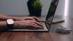 Person typing on laptop keyboard while wearing a smartwatch at a wooden desk.