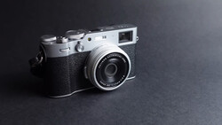 Fujifilm Instax rangefinder camera with silver top plate and black textured body against dark gray background.