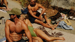 Group of people relaxing on a beach with scattered belongings and towels.