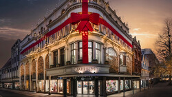 Historic corner building with ornate architecture illuminated at dusk, topped with large red ribbon bow.