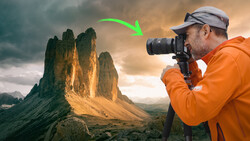 Photographer in orange jacket photographing dramatic mountain peaks during golden hour.