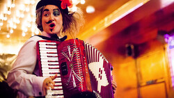 Performer playing a red and white accordion under warm stage lighting with an expressive facial expression.