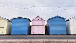 Three colorful beach huts in a row with blue and pink painted wooden facades and peaked roofs.