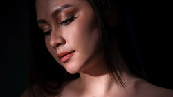 Woman's face in profile with warm golden eyeshadow and subtle lighting against dark background.