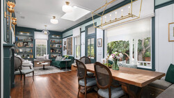Modern home office with dark teal walls, wooden desk, and large windows overlooking gardens.