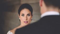 Bride in white lace wedding dress gazing at groom during intimate ceremony moment.