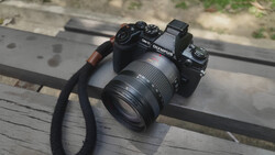 Olympus mirrorless camera with attached zoom lens and black camera strap on wooden surface.