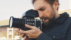 Photographer holding a Hasselblad medium format camera to his face while focusing on a subject.