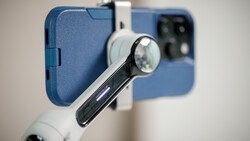 Macro lens attachment mounted on smartphone with blue case, showing optical magnification element close-up.