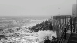 Dramatic seascape with crashing waves against a concrete seawall and rocky breakwater in stormy weather.