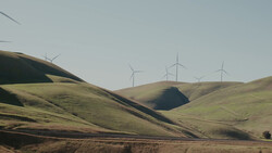 Rolling hills with wind turbines on distant ridge under overcast sky.