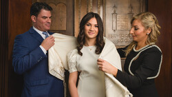 Three people examining a white garment in an ornate interior setting.
