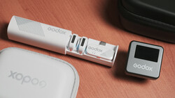 Godox camera lighting equipment arranged on a terracotta surface including a white cylindrical light, a small square transmitter, a white carrying pouch, and a black case.
