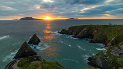 Dramatic sunset over dramatic coastal cliffs with turquoise waters and distant islands on the horizon.