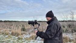 Videographer operating a camera mounted on a gimbal stabilizer in a snowy field.