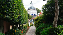 Manicured garden pathway lined with green hedges leading to a domed building with classical architecture.