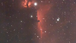 Deep-space photograph of an emission nebula with glowing red hydrogen gas clouds and scattered stars.
