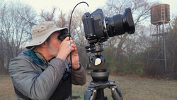 Photographer composing a shot through a large format camera mounted on a tripod in an open field.