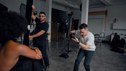 Photography crew adjusting lighting equipment during a studio shoot with a model in foreground.