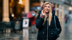 Woman in black winter jacket with colorful plaid hood talking on phone outdoors.