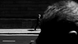 Man in business attire walking alone on a city street, shot in high-contrast black and white.