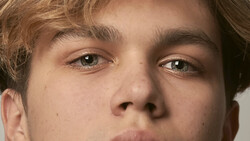 Close-up portrait of a young man with direct eye contact and neutral expression.