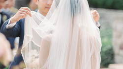 Groom adjusting bride's flowing veil during wedding ceremony.