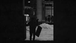 Silhouetted figure in dark coat holding briefcase, framed by building entrance in snowy urban setting.