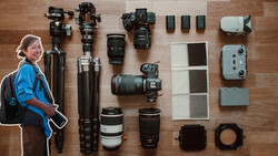 Photographer in blue jacket with complete camera gear laid out flat on wooden surface.