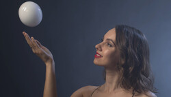 Woman in profile tosses a white sphere upward against a dark blue background.