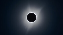 Total solar eclipse with moon silhouette centered against bright corona and darkened sky.
