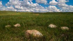Large boulders scattered across a green prairie under a partly cloudy sky.
