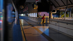 Lone figure in orange jacket standing on empty transit platform beneath arched ceiling.