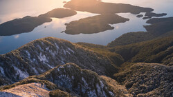 Forested mountains and islands at golden hour with still water reflecting the sky.