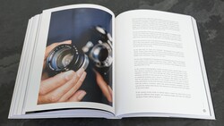Open book displaying a photograph of hands holding a vintage camera lens on the left page, with text on the right.
