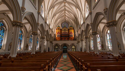Interior of a Gothic cathedral with soaring vaulted ceilings, ornate pipe organ, and stained glass windows lining both sides.