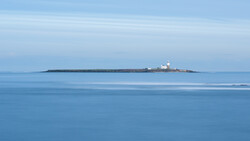 Small lighthouse on a rocky island beneath a clear blue sky and calm sea.