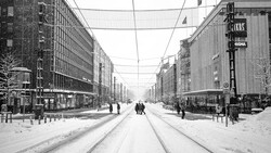 Snow-covered street with tram tracks stretching between tall residential buildings and storefronts.