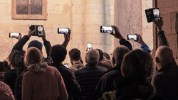 Crowd of people holding up smartphones to photograph a building facade.