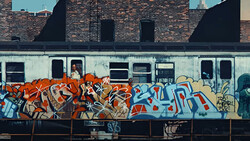 Vibrant graffiti mural on a train with orange, red, and blue lettering against weathered building backdrop.