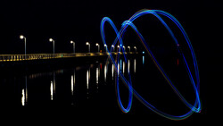 Long exposure photograph of a pier at night with blue light trails spiraling from its end.