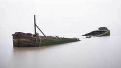 Two rusted, abandoned shipwrecks partially submerged in still water with algae-covered hulls.