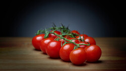 Cluster of ripe tomatoes with green stems on wooden surface against dark background.