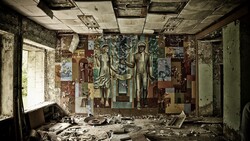 Abandoned interior room with deteriorating murals on walls and ceiling amid scattered debris and rubble.