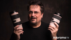 Photographer holding two telephoto lenses against a dark background.
